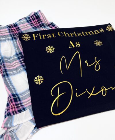 Personalised First Christmas short pyjamas with married name and gold snowflake design, folded with pink and blue check shorts – festive newlywed gift.