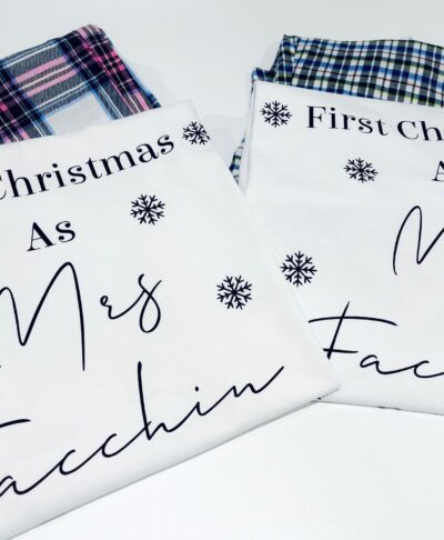 Close up of two personalised white pyjama tops with check bottoms visible behind them. The text on the left reads 
