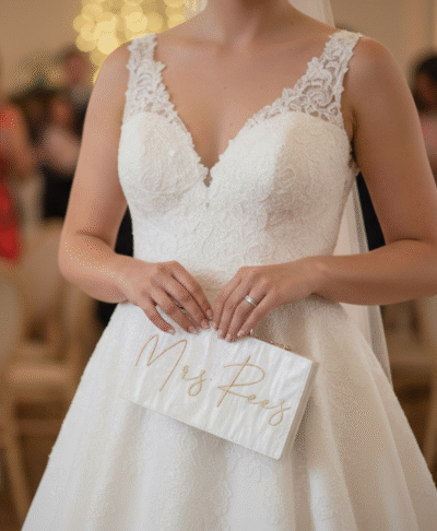 Close up of a bride holding a personalised white "Mrs Rees" wedding clutch bag at a relaxed evening reception, perfect for bridal accessories.