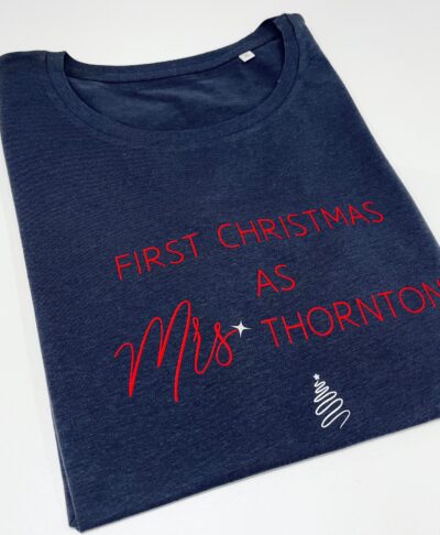 A dark grey folded t-shirt featuring Christmas themed text printed in red and white. The text reads: 