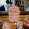 Clear acrylic sign reading “Love is Sweet Please Take a Treat” displayed on a wedding sweet table with jars of colourful sweets.
