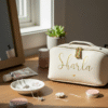Personalised ivory vegan leather makeup bag or jewellery travel case with the name 'Sharla' in gold script, styled on a wooden vanity with luxury cosmetics and a silver necklace.